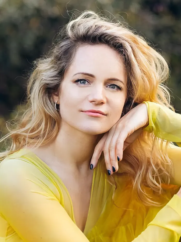 Agnės Doveikaitės portretas, ji švelniai šypsosi gamtos fone.